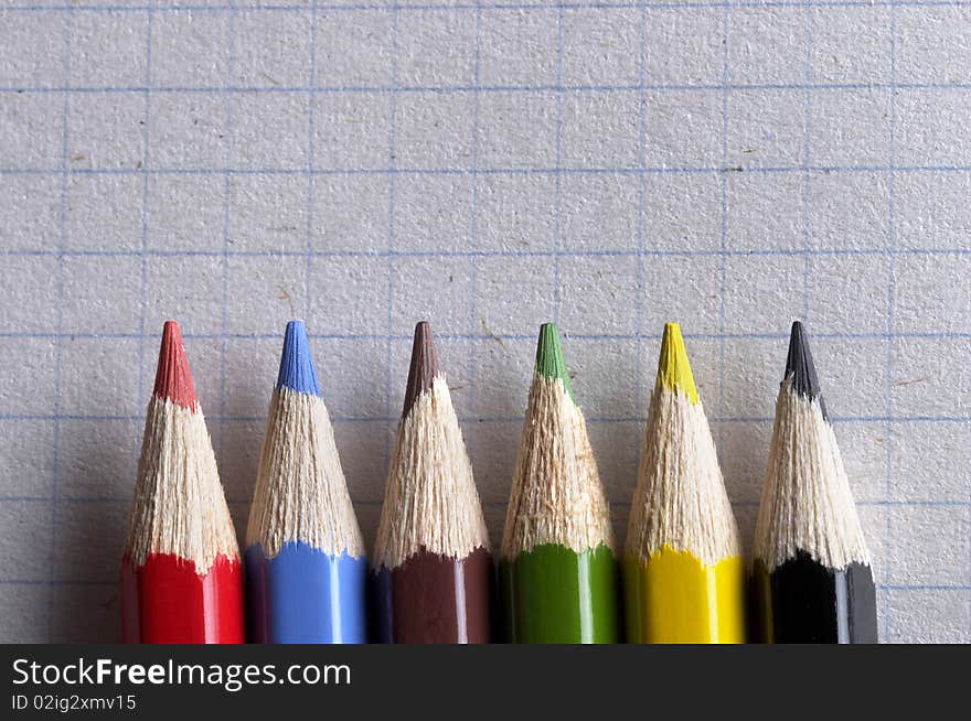 Colorful pencils set macro shot over checked paper background