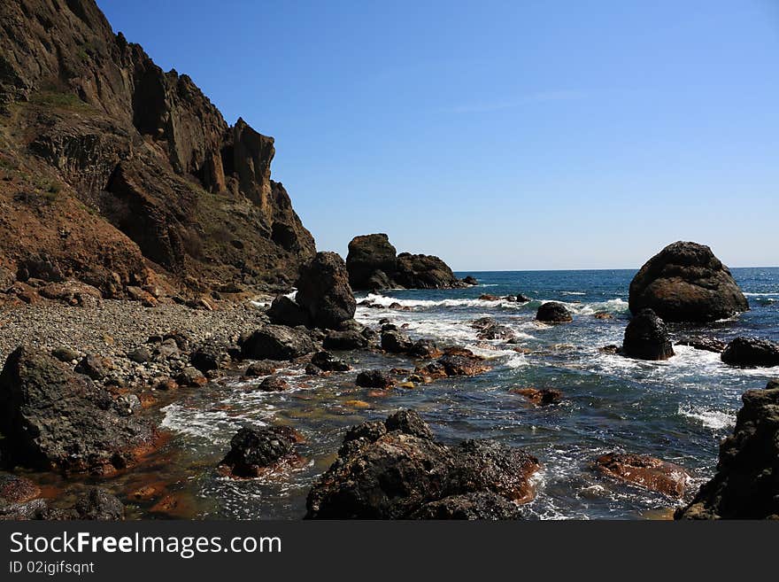 Seascape - a beautiful beach, sea and sky. In the foreground  stones from the vent of an ancient volcano karadag. Seascape - a beautiful beach, sea and sky. In the foreground  stones from the vent of an ancient volcano karadag