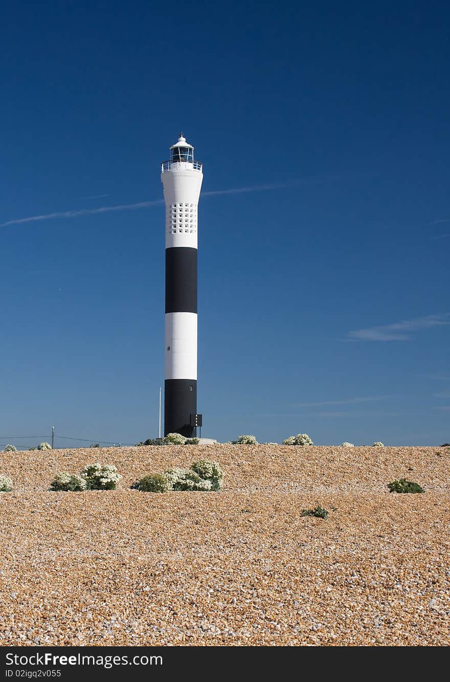 Dunguness Lighthouse against a clear blue sky with a shingle beach. Dunguness Lighthouse against a clear blue sky with a shingle beach