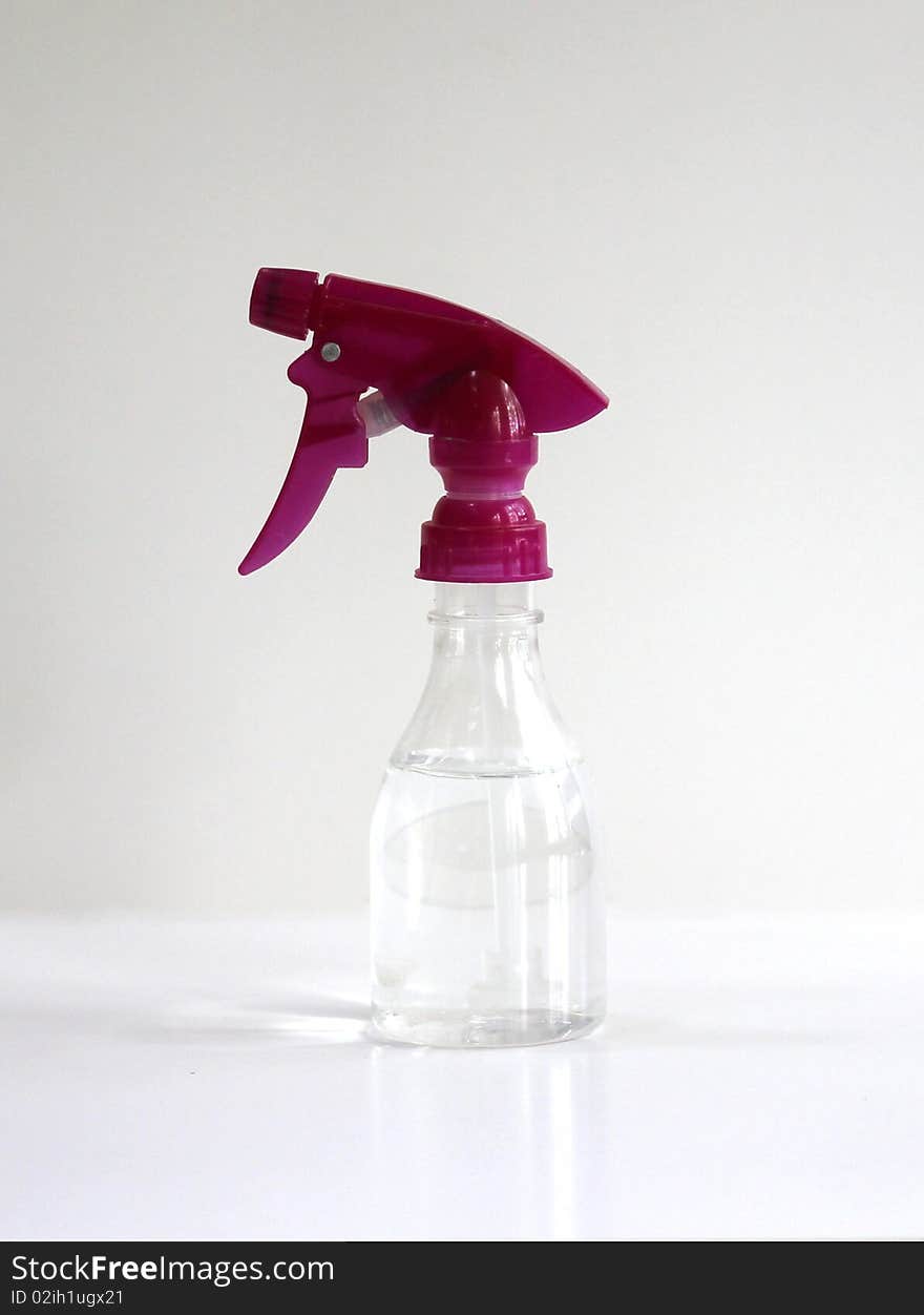 A clear spray bottle with a pink nozzle with a white background.