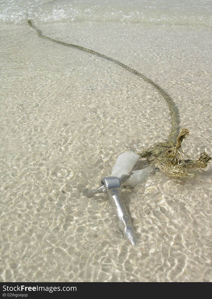 The sea anchor is in the clear sea water. You can see through the sea water. The beach has a white sand.