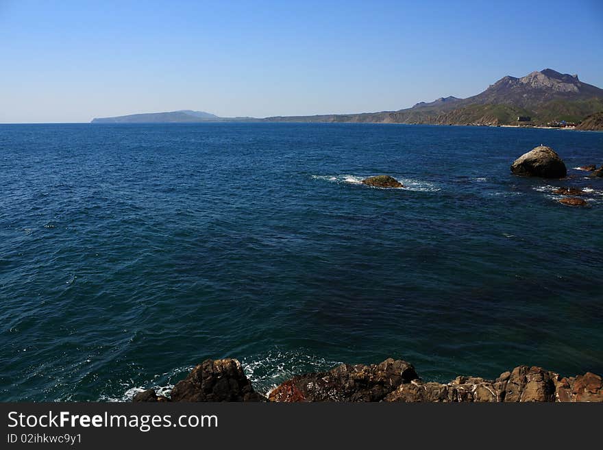 Seascape - a beautiful beach, sea and sky. In the foreground stones from the vent of an ancient volcano karadag. Seascape - a beautiful beach, sea and sky. In the foreground stones from the vent of an ancient volcano karadag