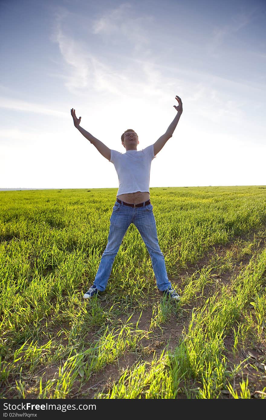 Young man stay in green field with hands up