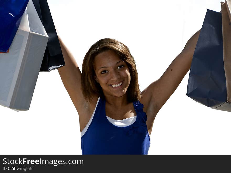 Multi race teenage girl with her arms holding up several shopping bags, smiling, happy shopper, accent of sun highlights along side of cheek. wearing a bright blue layered white tank top. white back ground. Multi race teenage girl with her arms holding up several shopping bags, smiling, happy shopper, accent of sun highlights along side of cheek. wearing a bright blue layered white tank top. white back ground.