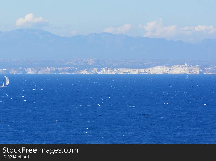 Straits of Bonifacio (Bocche di Bonifacio), strait between Sardinia (Italy) and Corsica (France) which divides the Tyrrhenian Sea from western Mediterranean Sea, and view of Bonifacio cliffs and mountains in the background. Straits of Bonifacio (Bocche di Bonifacio), strait between Sardinia (Italy) and Corsica (France) which divides the Tyrrhenian Sea from western Mediterranean Sea, and view of Bonifacio cliffs and mountains in the background