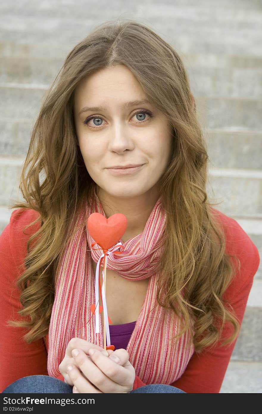 Beautiful girl in the street sitting on the stairs in the hands of a red heart on the wooden stick. Beautiful girl in the street sitting on the stairs in the hands of a red heart on the wooden stick