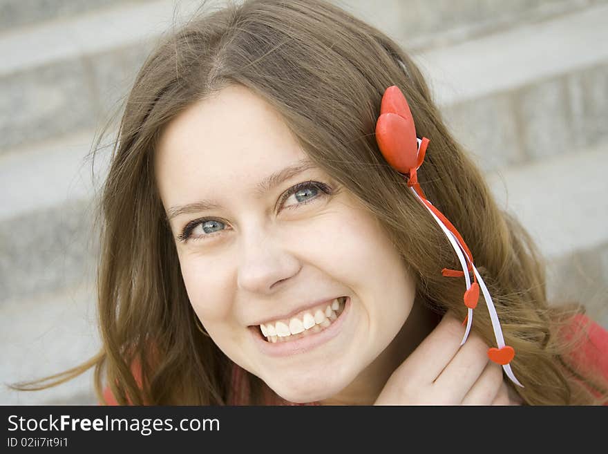 Beautiful girl in the street sitting on the stairs in the hands of a red heart on the wooden stick. Beautiful girl in the street sitting on the stairs in the hands of a red heart on the wooden stick