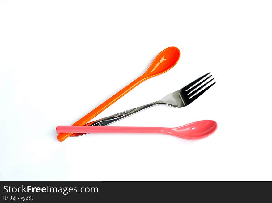 A pair of colorful plastic spoons with a stainless steel fork in the middle isolated on white background. A pair of colorful plastic spoons with a stainless steel fork in the middle isolated on white background