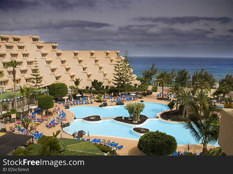 Occidental hotel at lanzarota with a big swimming pool with people sunbathing surrounded by palmtrees. Occidental hotel at lanzarota with a big swimming pool with people sunbathing surrounded by palmtrees