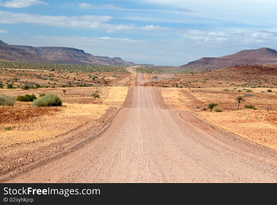 Straight sandy road through Namibian landscape with blue cloudy sky. Straight sandy road through Namibian landscape with blue cloudy sky.