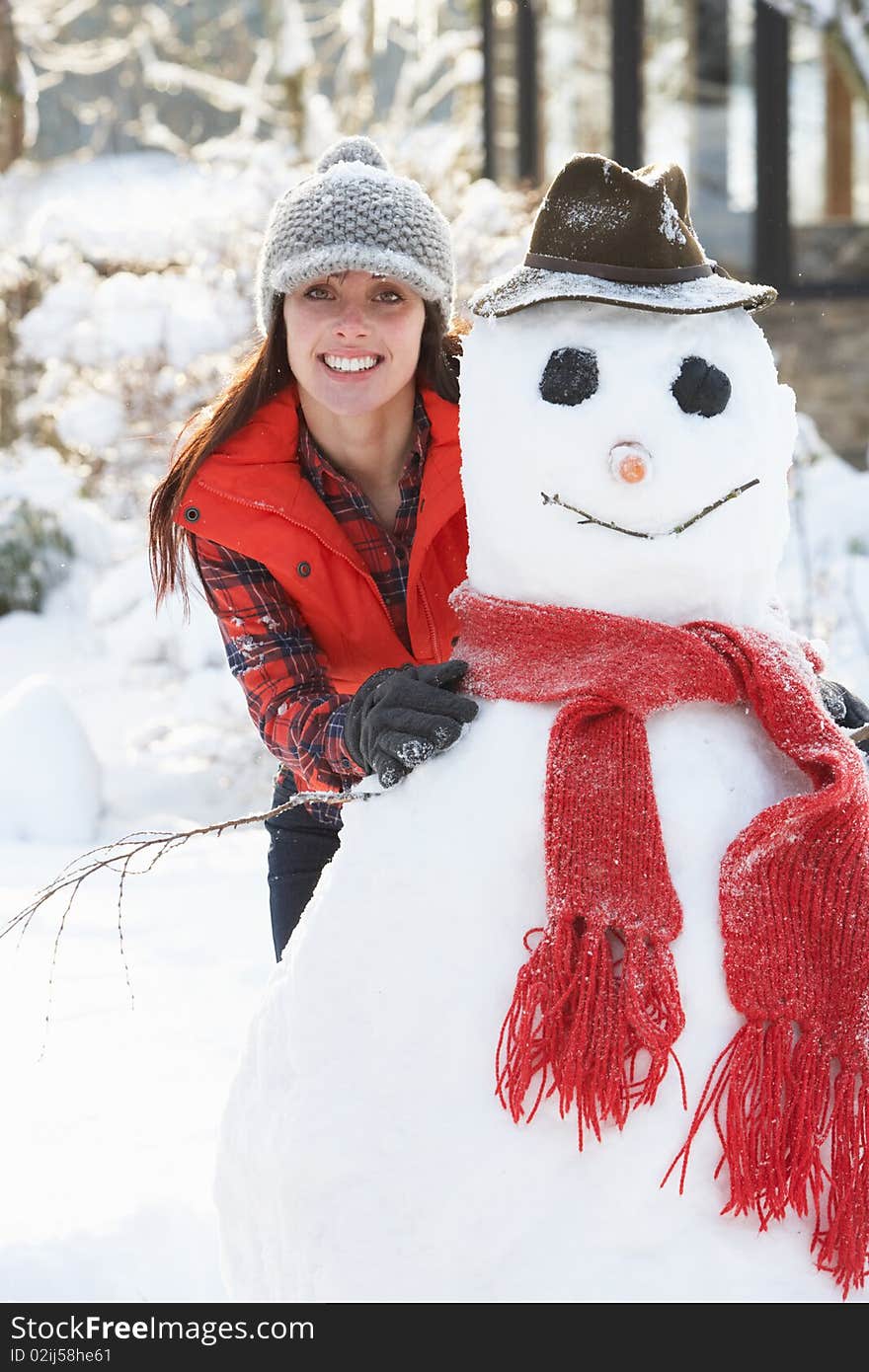 Young Woman Building Snowman In Garden Smiling