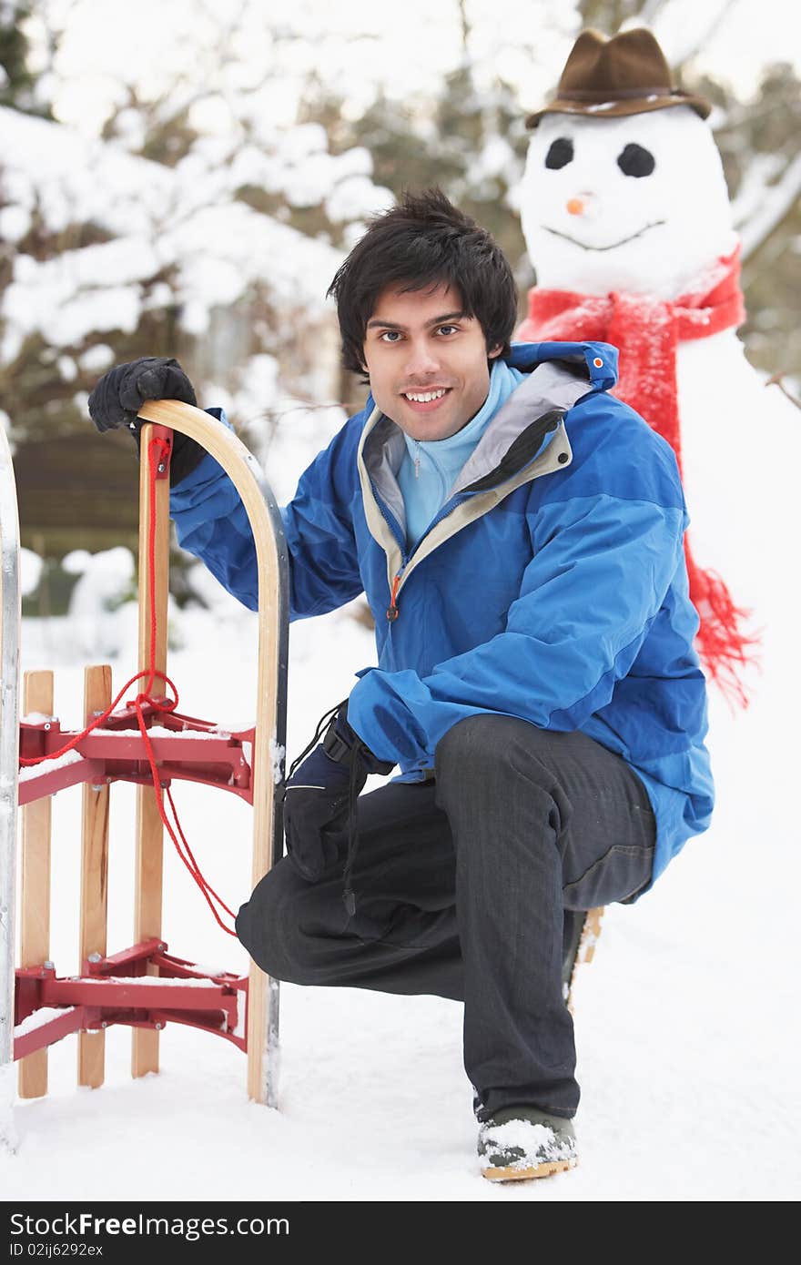 Smiling Teenage Boy With Sledge Next To Snowman