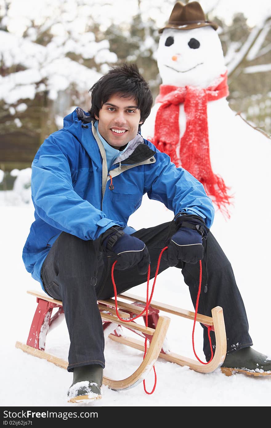 Smiling Teenage Boy With Sledge Next To Snowman