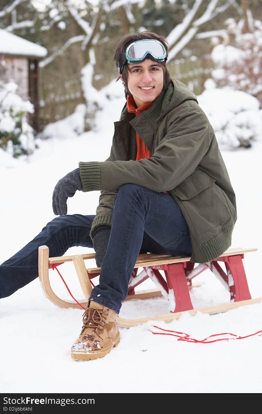 Teenage Boy With Sledge Next To Snowman Smiling At Camera