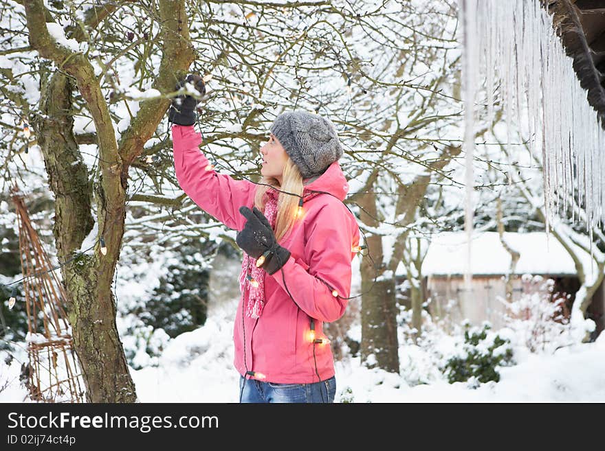 Teenage Girl Hanging Fairy Lights In Tree With Icicles In Foreground