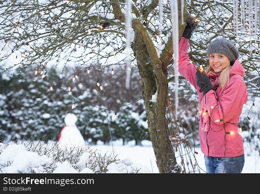 Teenage Girl Hanging Fairy Lights In Tree With Icicles In Foreground