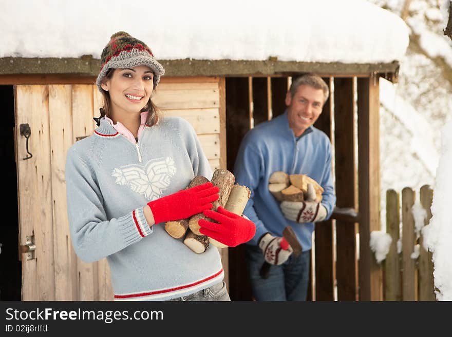 Young Couple Collecting Logs From Wooden Store In Snow