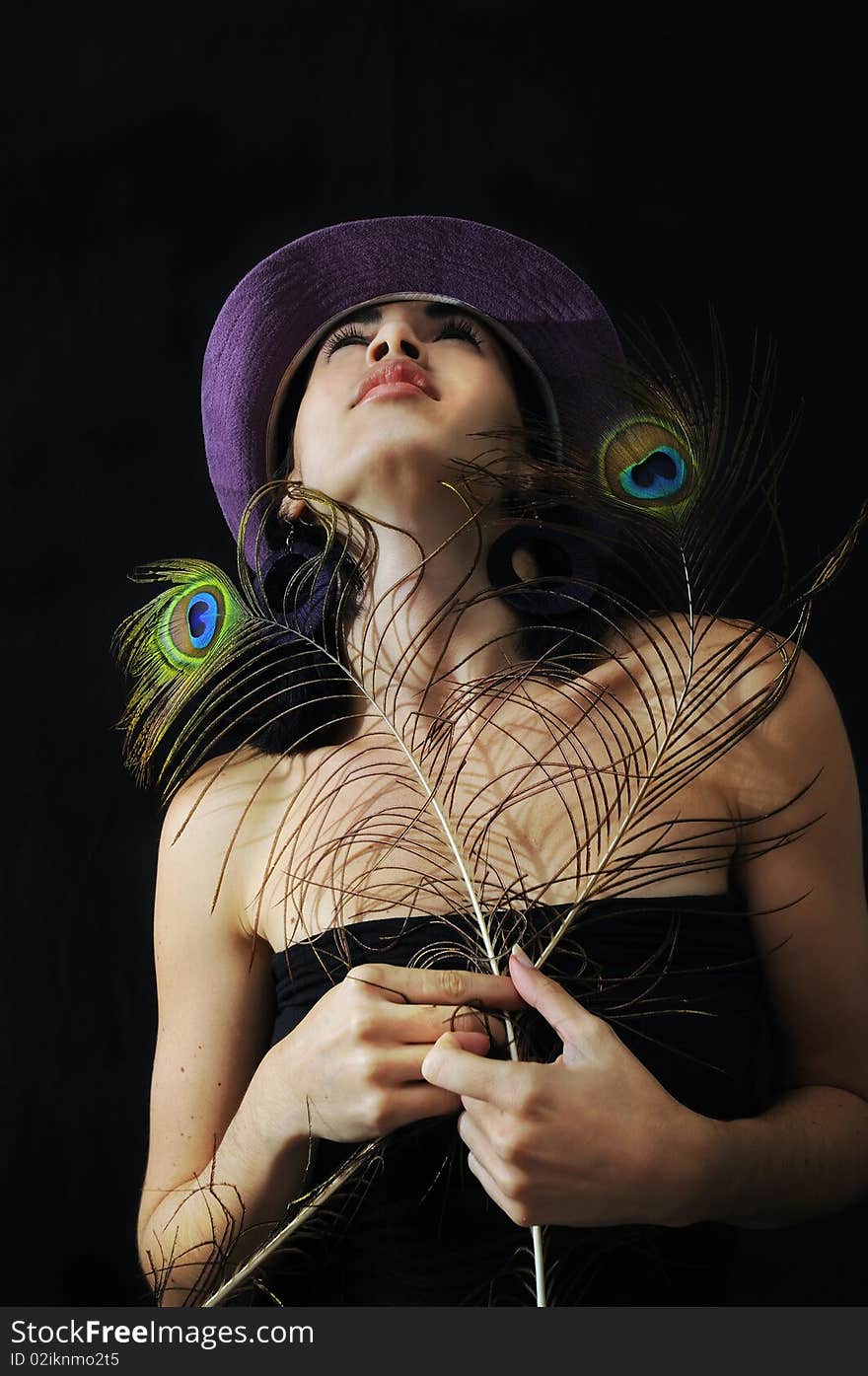 Portrait of young trendy girl holding peacock feathers against black background. Portrait of young trendy girl holding peacock feathers against black background