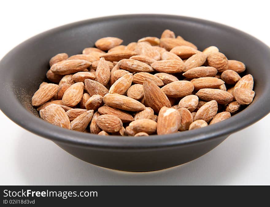 A black bowl full of salted almonds isolated on a white background. A black bowl full of salted almonds isolated on a white background