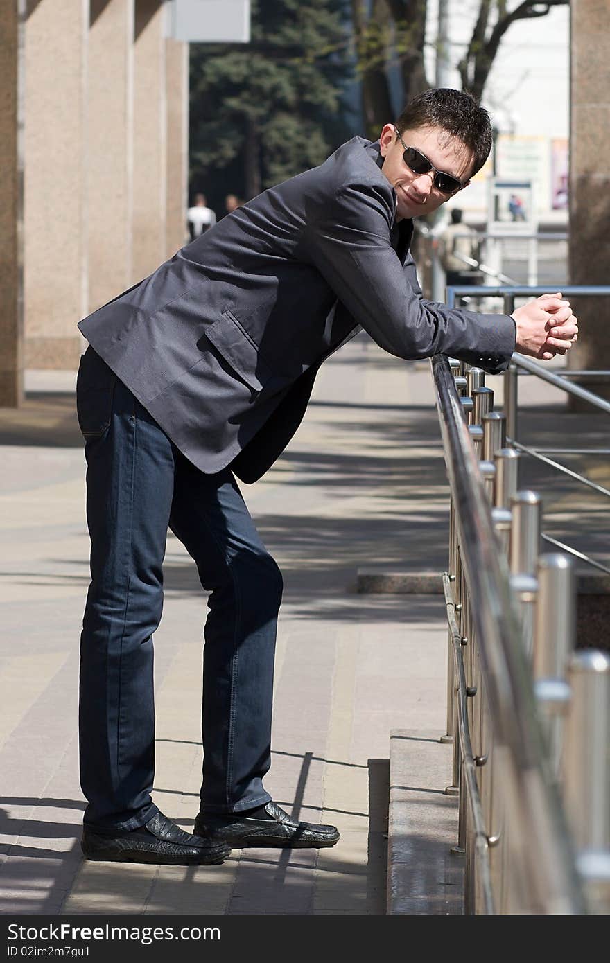 Young european businessman leans on handrails near the office building with columns smiling. Young european businessman leans on handrails near the office building with columns smiling