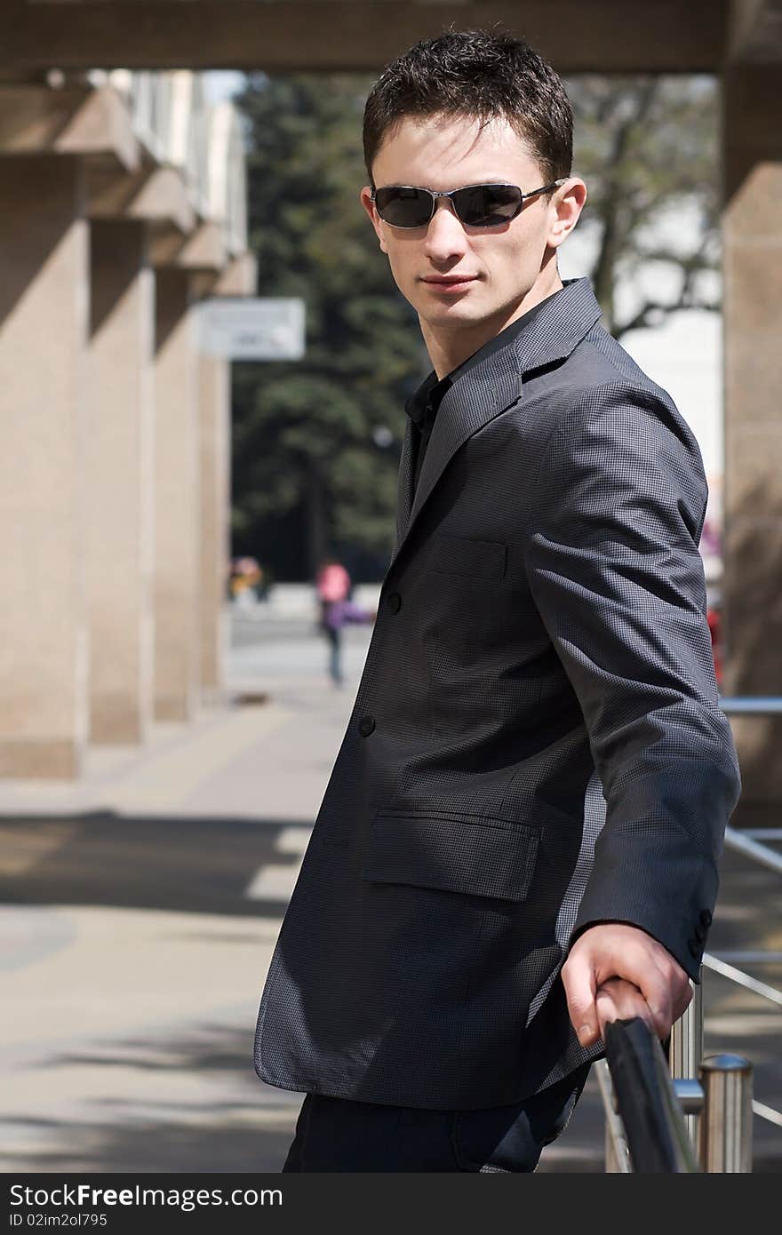 Young confident man leans on metal handrails near the office building with columns. Young confident man leans on metal handrails near the office building with columns