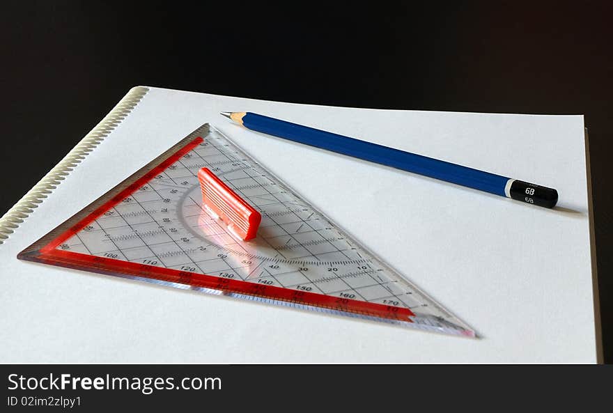 Blue pen and set square on white paper with black background