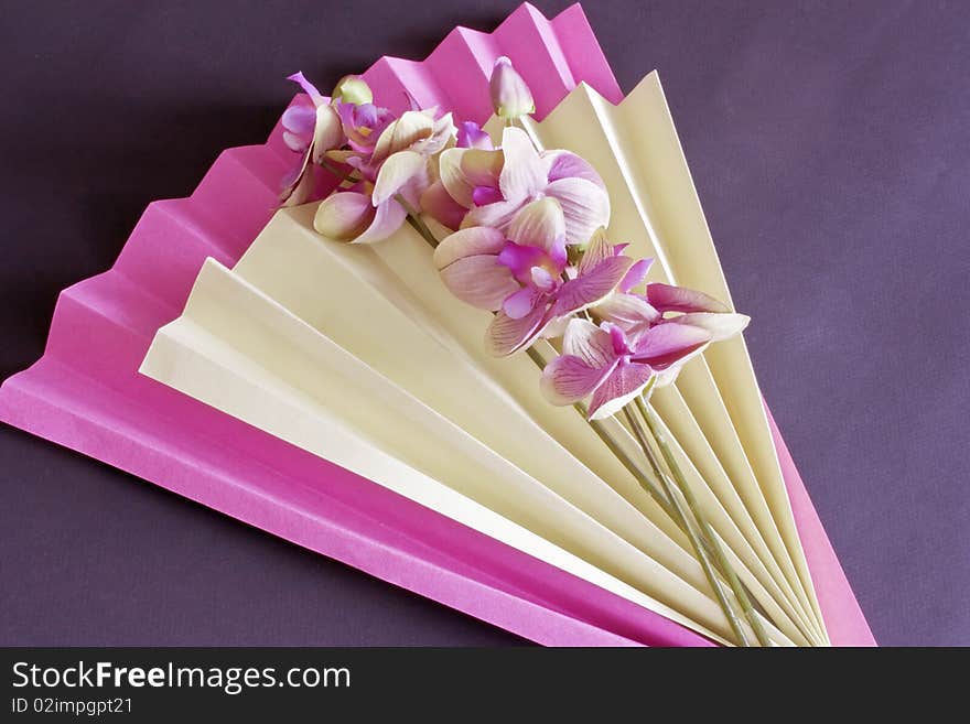 A pink and yellow foled paper fan and  silk orchids. A pink and yellow foled paper fan and  silk orchids