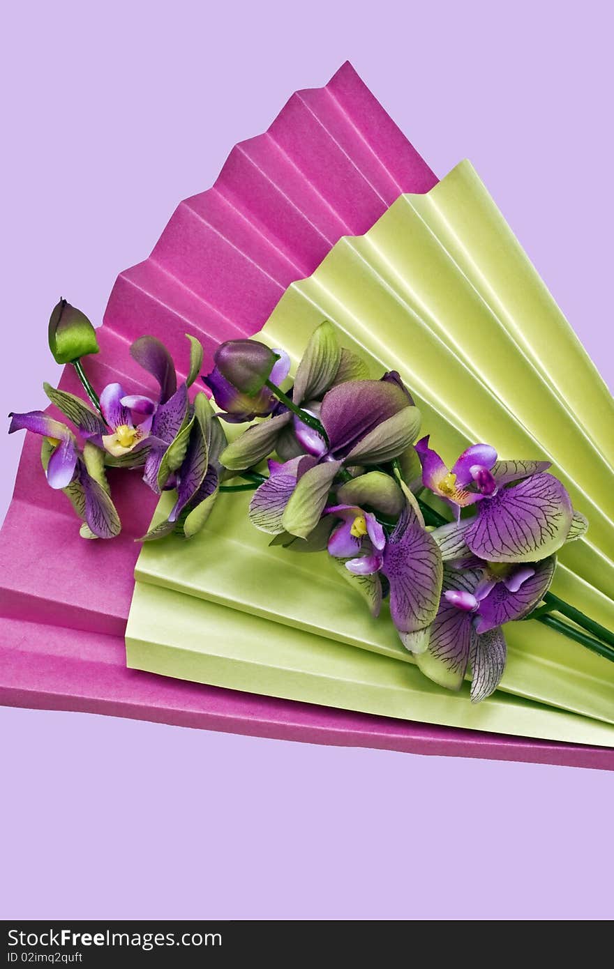 A pink and yellow folded paper fan and silk orchids. A pink and yellow folded paper fan and silk orchids