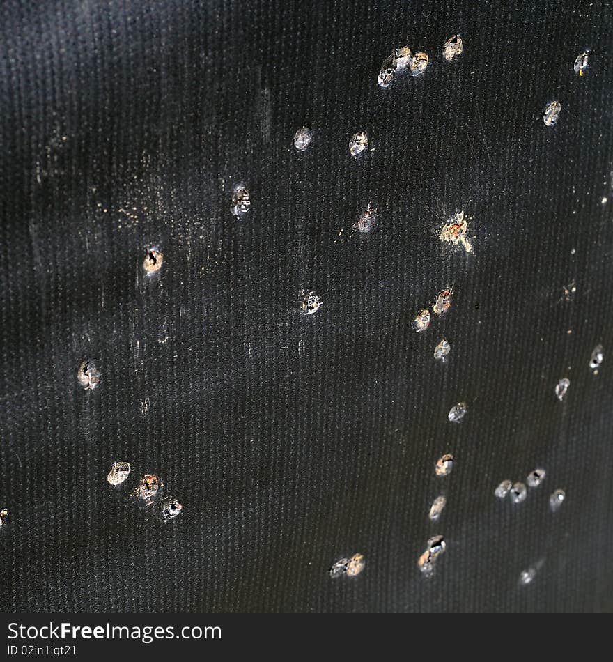 Arrow holes in black tarp practice target for archery. It also looks liek bullet holes