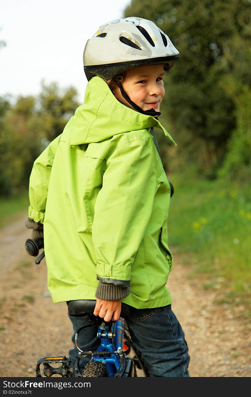 5 years old boy looking back over his shoulder while stopped on his bike, with helmet and green vest. 5 years old boy looking back over his shoulder while stopped on his bike, with helmet and green vest