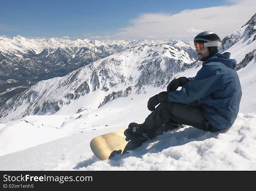 Young snowboarder in blue jacket sitting on the snow. High mountains view. Young snowboarder in blue jacket sitting on the snow. High mountains view