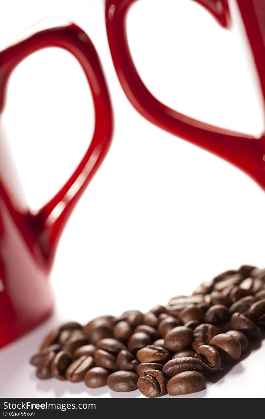 Coffee-beans heart against red cup`s handles on white backround