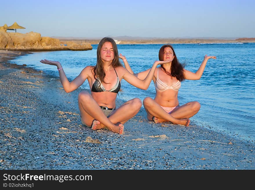 Beautiful young girls practicing yoga  during sunrise  at sea coast