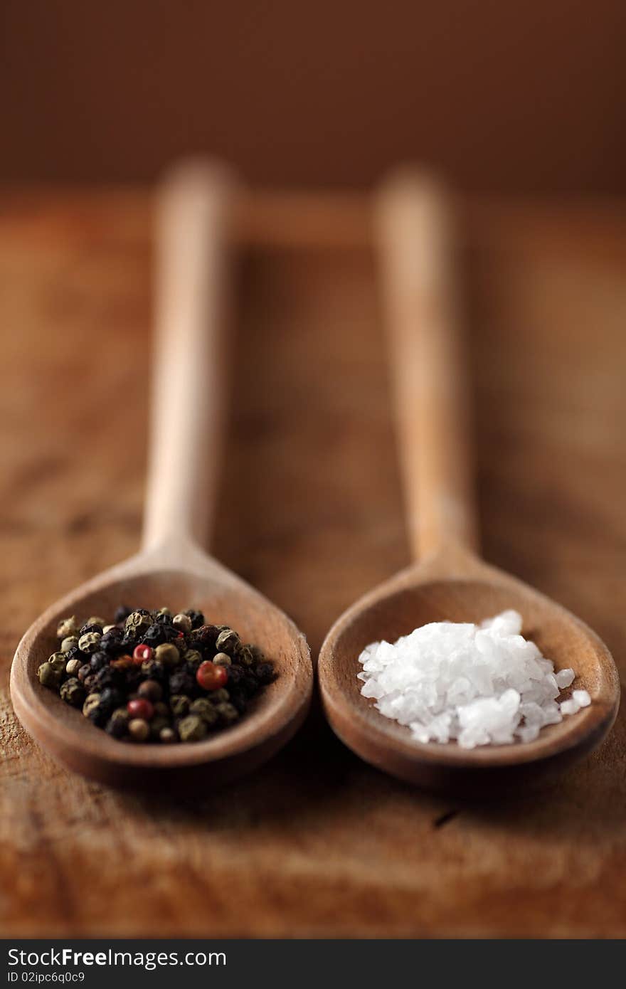 Salt and pepper grains on wooden spoon on a old wooden table