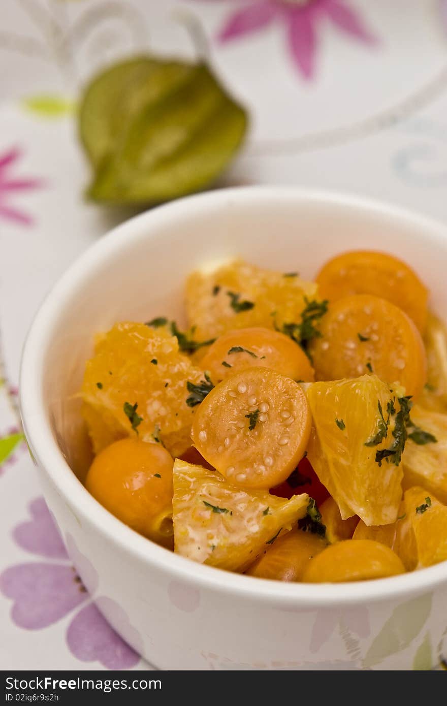 Fruit salad made of oranges, physallis, mint and whipped cream against a flowery background.