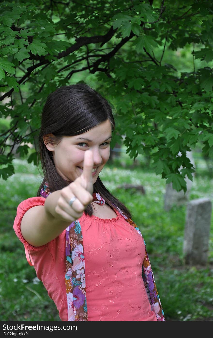 Young beautiful girl holding a thumb up in a background of nature. Young beautiful girl holding a thumb up in a background of nature