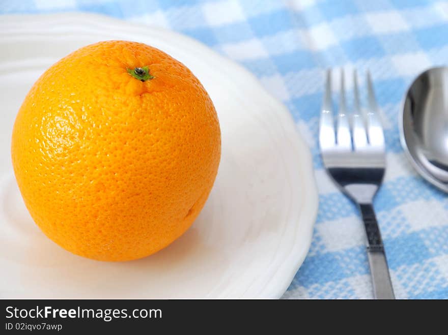 Closeup of orange on plate with utensils. Healthy eating and lifestyle, diet and nutrition, and fresh fruit concepts . Closeup of orange on plate with utensils. Healthy eating and lifestyle, diet and nutrition, and fresh fruit concepts .