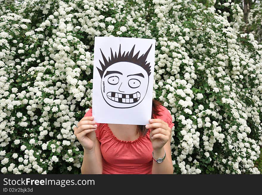 Beautiful girl holding a paper with a drawn face e