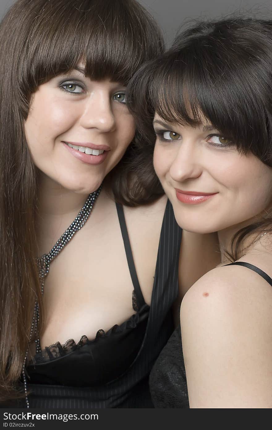 Two smiling girls in black dresses on dark background