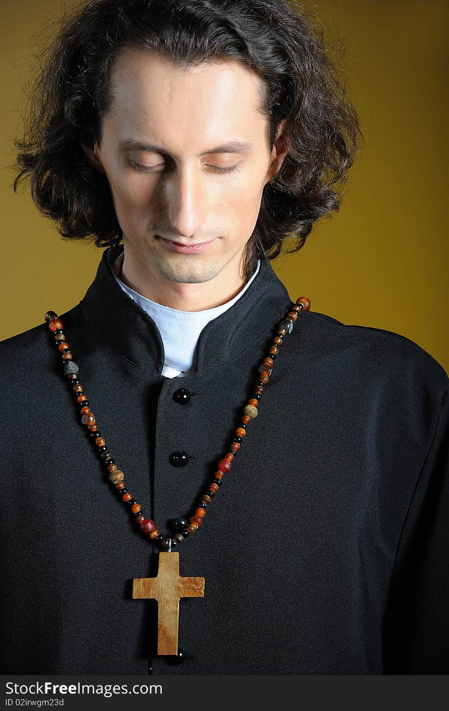 Conceptual portrait of Praying priest with wooden cross praying. yellow background