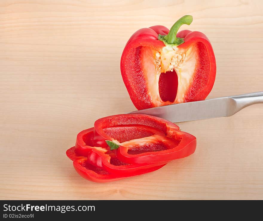 Red bell pepper sliced with a knife on a cutting board