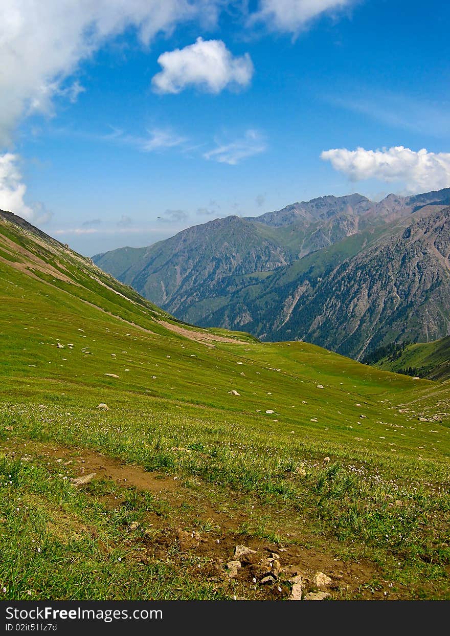 Summer mountains at Shymbulak Ski resort near Almaty, Kazakhstan, with green grass and blue sky