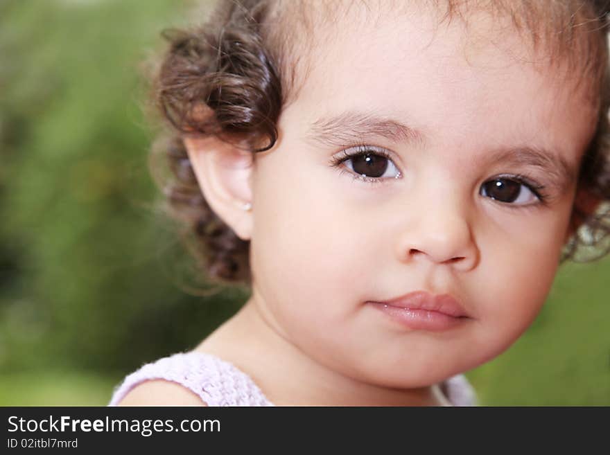 Beauty baby looking at camera over green background. Outdoor image