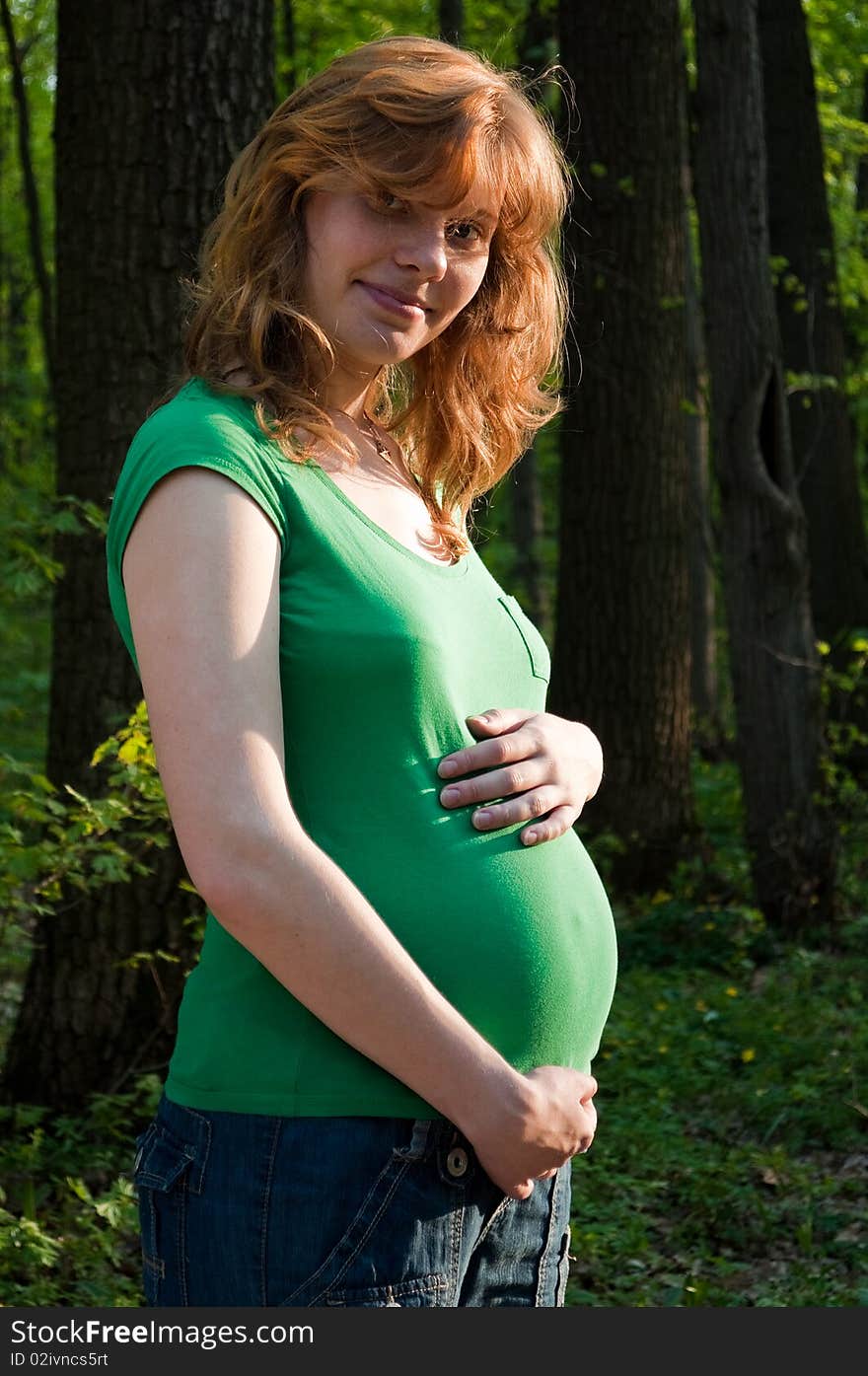 Happy young pregnant woman holding her hands on her tummy