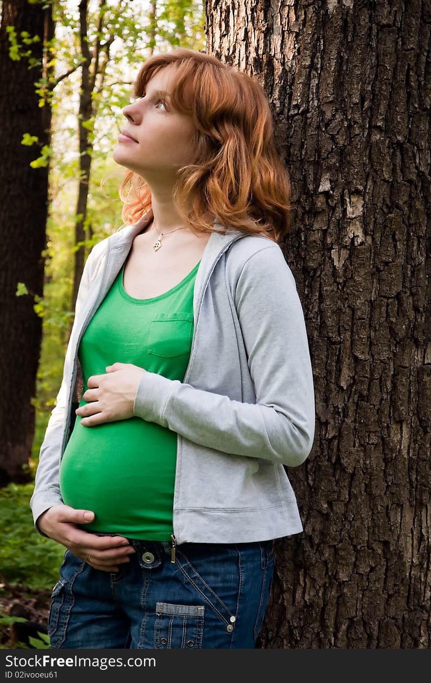 Happy young pregnant woman holding her hands on her tummy