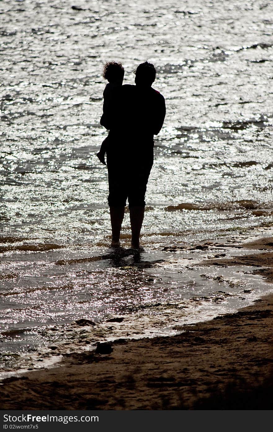 View of a mother holding a child on the shore of the beach. View of a mother holding a child on the shore of the beach.