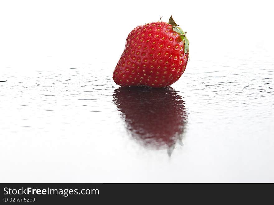 Single ripe fresh strawberry on wet dark reflecting surface with water drops