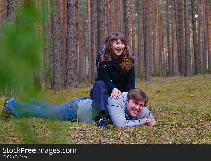 Portrait of a cheerful laughing couple - he is lying on a grass and she is sitting on his back. Portrait of a cheerful laughing couple - he is lying on a grass and she is sitting on his back