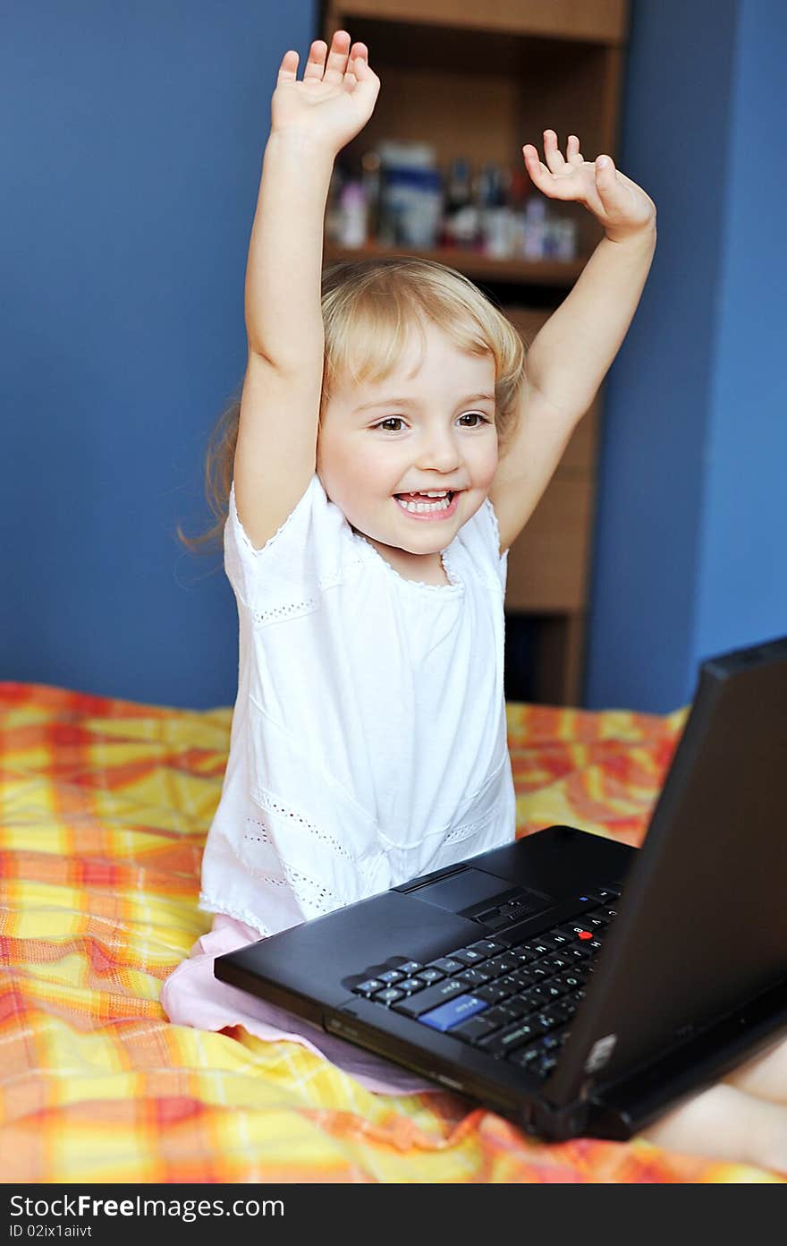 Cheerful little girl with laptop sits on bed of parents