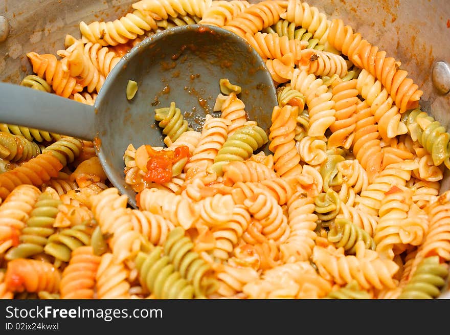 A big pot of pasta covered with tomato sauce with ladle